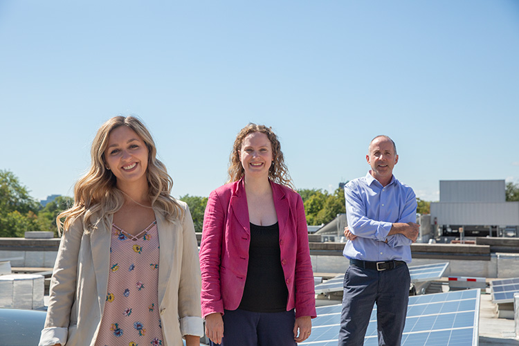 Three members of the Sustainability Office team standing on a solar panel roof on-campus.