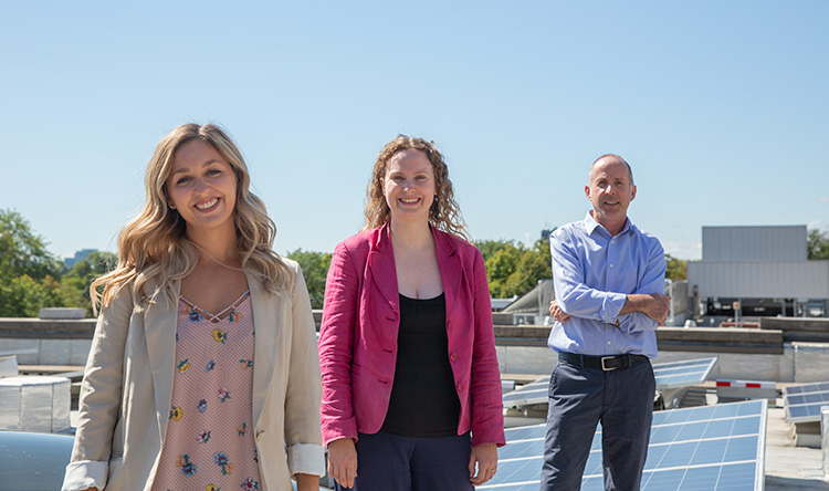 Three members of the Sustainability Office team standing on a solar panel roof on-campus.
