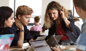 An associate professor talks to three students sitting at a table.