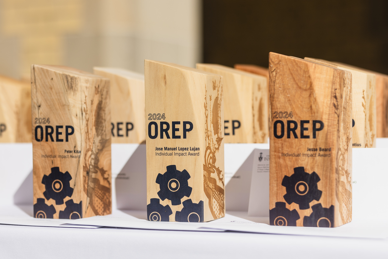 A photo of the new awards statues lined up on a table with a white table cloth. They are wooden blocks with OREP and a graphic of gears printed on them, with a design burned onto the other side.