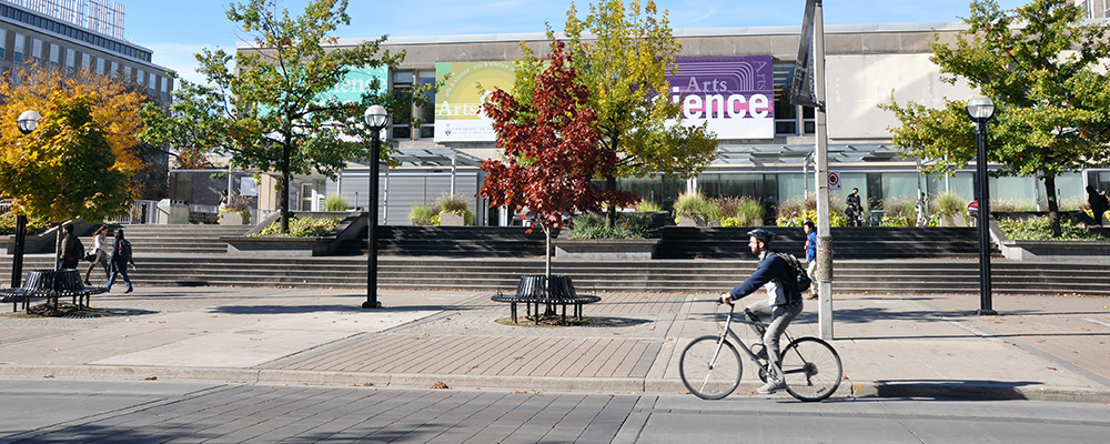 A person biking on campus in front of Sidney Smith Hall.