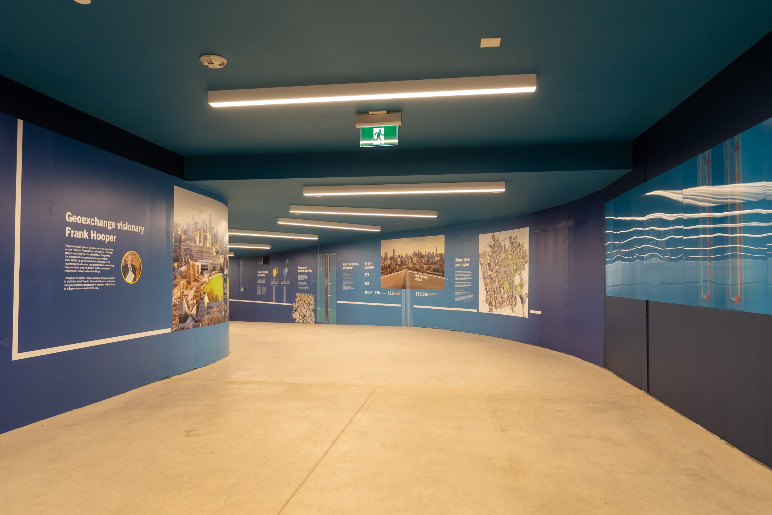 A view of a long, curved hallway underground, with a blue roof, and blue panel displays along the hall, museum style.