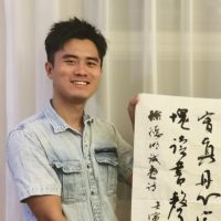 A work-study student holds up a poster display of characters written in ink.